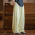 Person wearing light-colored wide-leg pants and a dark top against a wooden background